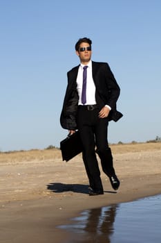 Close up view of a bunisess man in a dark suit walking on the beach.