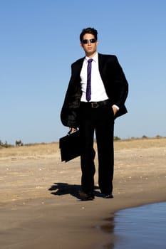 Close up view of a bunisess man in a dark suit walking on the beach.