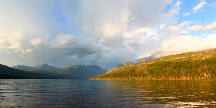 Sunlight illuminates the shoreline of Kintla Lake against a stormy sky in Glacier National Park - USA.