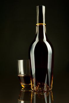 A bottle and a glass of cognac in a black background