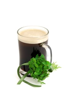 Dark beer in glass and bouquet of false shamrock (Oxalis) with green ribbon on white background