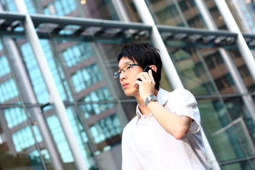 young businessman in a suit holding mobile phone in front of modern building 