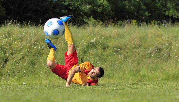 A soccer player on the ground after he kicked the ball in an acrobatic position.