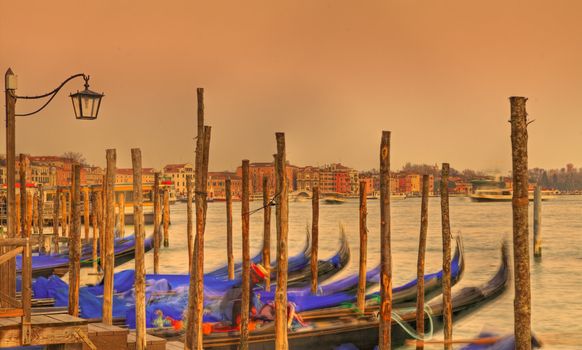 Sunset colors in Venice with gondolas in first plane and specific architecture in the distance.