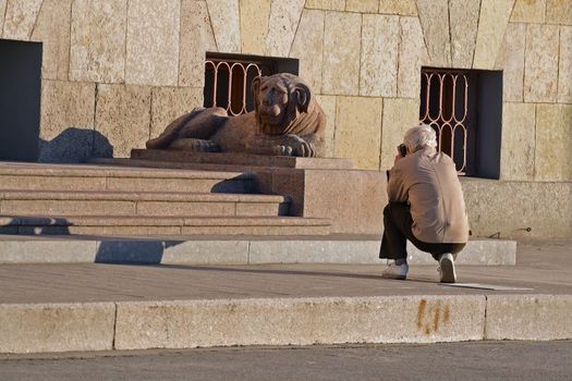 Hiker take a photograph granite sculpture lion on river's Neva embankment in Saint-Petersburg, Russia.