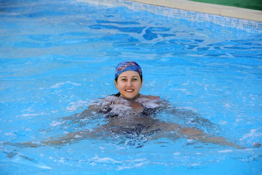 Beautiful young smiling girl sailling in pool in blue kerchief