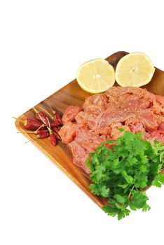 raw pork meat with red pepper, lemon and parsley ready to be cooked on a wooden tray (over white)
