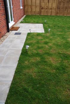 beautiful back yard garden (green grass, wood fence/door, stone pavement, solar panel lights and brick wall)