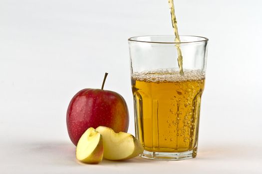 Apple cider pouring down into glass with apples at the side. On white background
