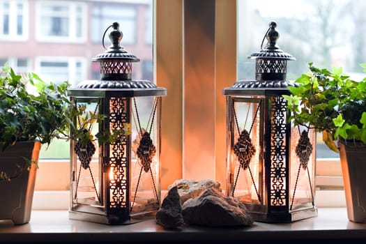 Lanterns with burning candles in window on rainy winterday - homelike inside, cold outside
