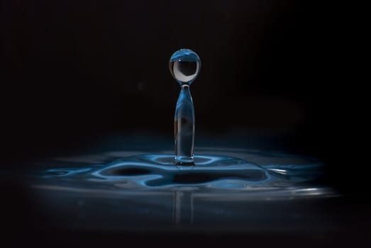 Clean blue drop of water splashing in clear water. Abstract blue environmental background.