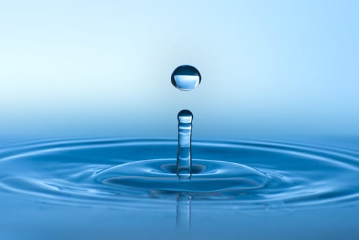 Clean blue drop of water splashing in clear water. Abstract blue environmental background.