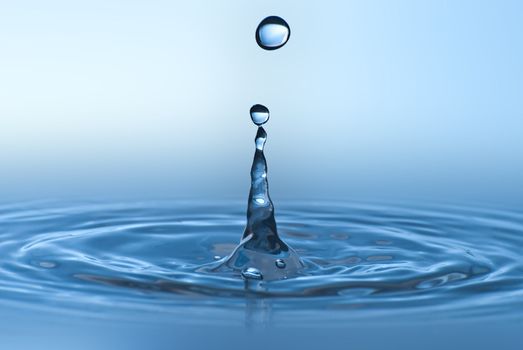 Clean blue drop of water splashing in clear water. Abstract blue environmental background.