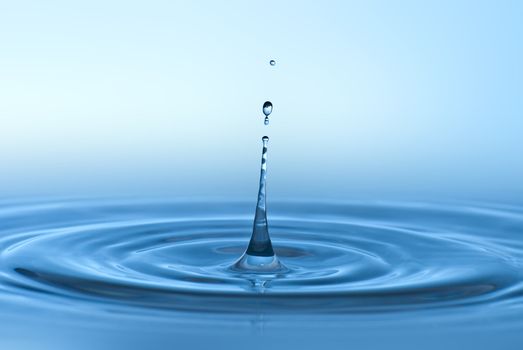 Clean blue drop of water splashing in clear water. Abstract blue environmental background.