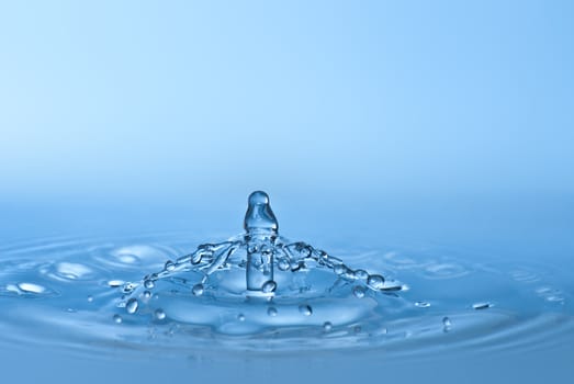 Clean blue drop of water splashing in clear water. Abstract blue environmental background.