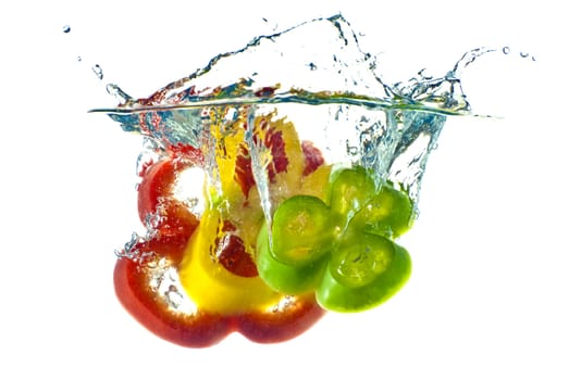 Red, yellow and green abstract pepper splashing in clear blue water - isolated against white background.