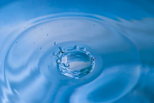 Clean blue drop of water splashing in clear water. Abstract blue environmental background.