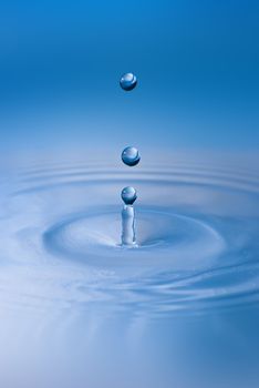 Clean blue drop of water splashing in clear water. Abstract blue environmental background.