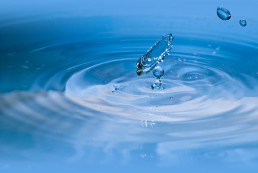 Clean blue drop of water splashing in clear water. Abstract blue environmental background.