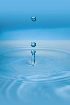 Clean blue drop of water splashing in clear water. Abstract blue environmental background.