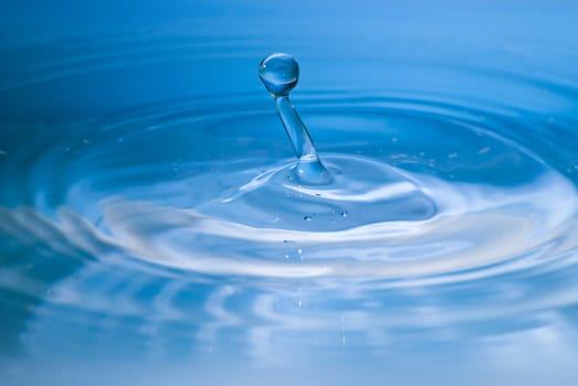 Clean blue drop of water splashing in clear water. Abstract blue environmental background.