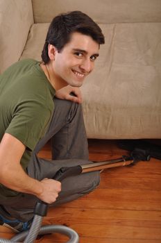 smiling young man with vacuum cleaner doing the housework