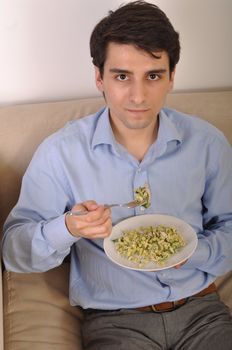 attractive young man sitting on the couch eating lunch (pasta with chicken)