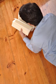 back view of a young man reading a business book while lying on the floor at home