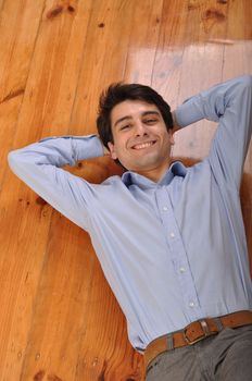 smiling attractive young man lying on wooden floor at home