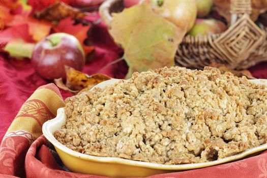 Freshly baked apple crisp with fresh apples and autumn leaves in the background. Shallow depth of field with selective focus on the foreground.