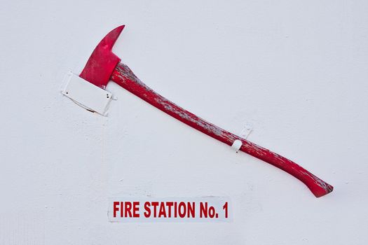 A red axe hanging on a white wall of a fire station. There is also a Fire Station sign in red letters.