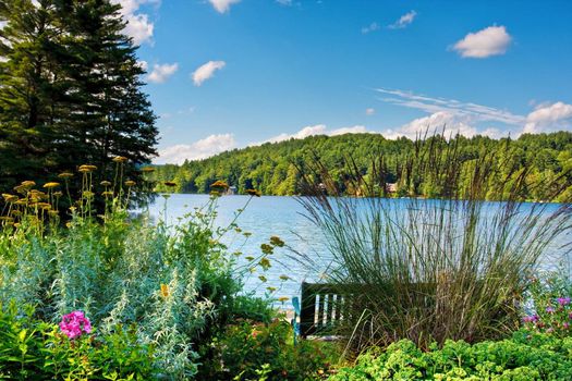 A scenic lake in the mountains. There is a bench and a flower garden in the foreground.