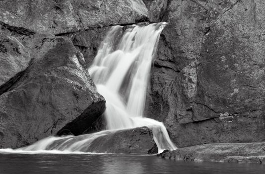 A waterfall over stone emptying into calm water below. Photo is in black and white.