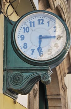 green antique wall clock hanging on a street building