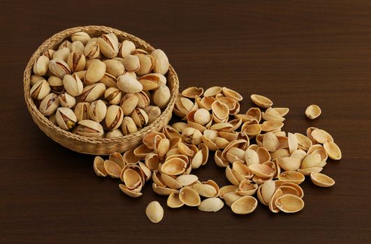 Pistachios in interwoven bowl with spilled nutshells on dark wooden table