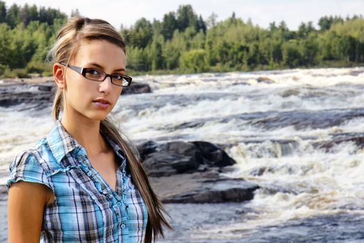 Young friendly brunette looking at camera in front of beautiful white waters waterfall landscape.