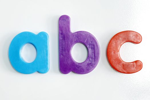 Fridge magnet: colorful plastic alphabet letters on textured white refrigerator.