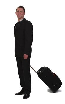 A young smiling businessman carrying a roller suitcase, isolated against a white background.