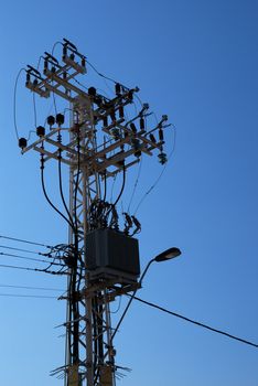 Electric transformer and lamp on pillar over blue sky 