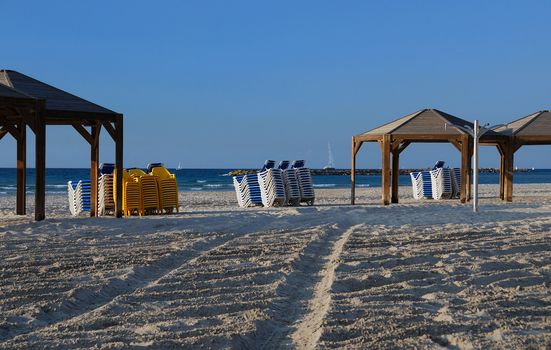 End of beach season - empty beach with accurate piles of color plastic chairs and chaise-longue
