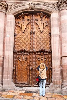 A woman stops to photograph a massive and ornate colonial door in a church in San Miguel Allende, Mexico