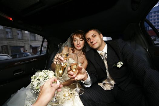 Newly-married couple with glasses of champagne in the automobile
