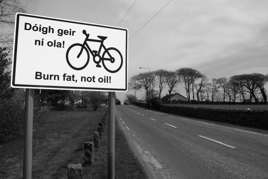 burn fat not oil irish road sign on a quiet road entering a town in ireland in black and white