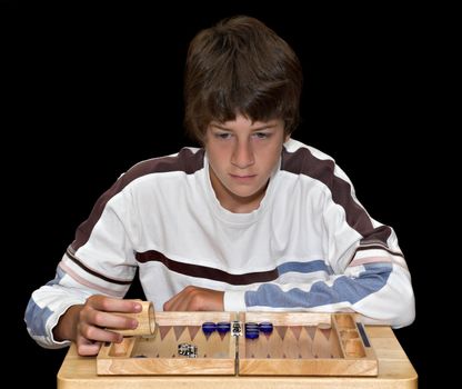 A young teenage boy playing a game of backgammon. The boy and board are isolated over a black background.