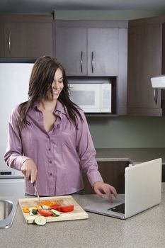Young woman trying to cut vegetables and working on a laptop