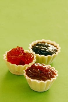 three kinds of jam in small edible treats over light green background