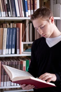 A young college aged man reading a book at the library.