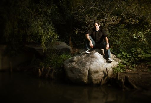 A man in a dark forest, sitting on a rock