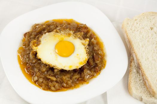 Delicious stew with baked onion, egg and sausages served on table with two slices of bread