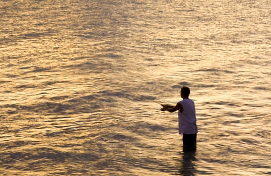 Silhouette of a man fishing in the sea as the sun turns the ocean into a bright yellow